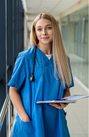 A nurse in blue scrubs with a stethoscope, holding patient notes in a hospital corridor